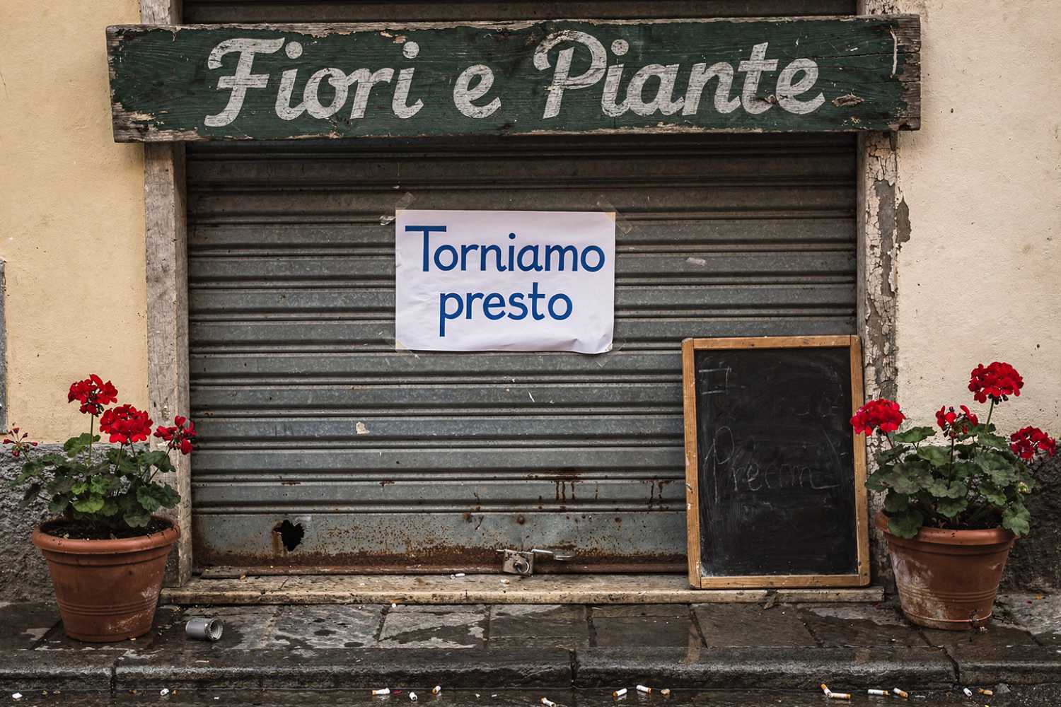 Saracinesca abbassata di un negozio di fiori con un avviso scritto a mano e le piante ancora curate all'ingresso